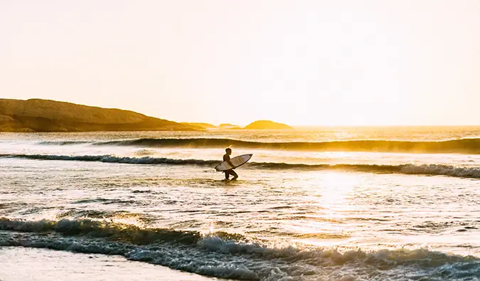 Isang nag-iisang manlalakbay na nagsu-surf sa South Africa habang lumulubog ang araw sa background