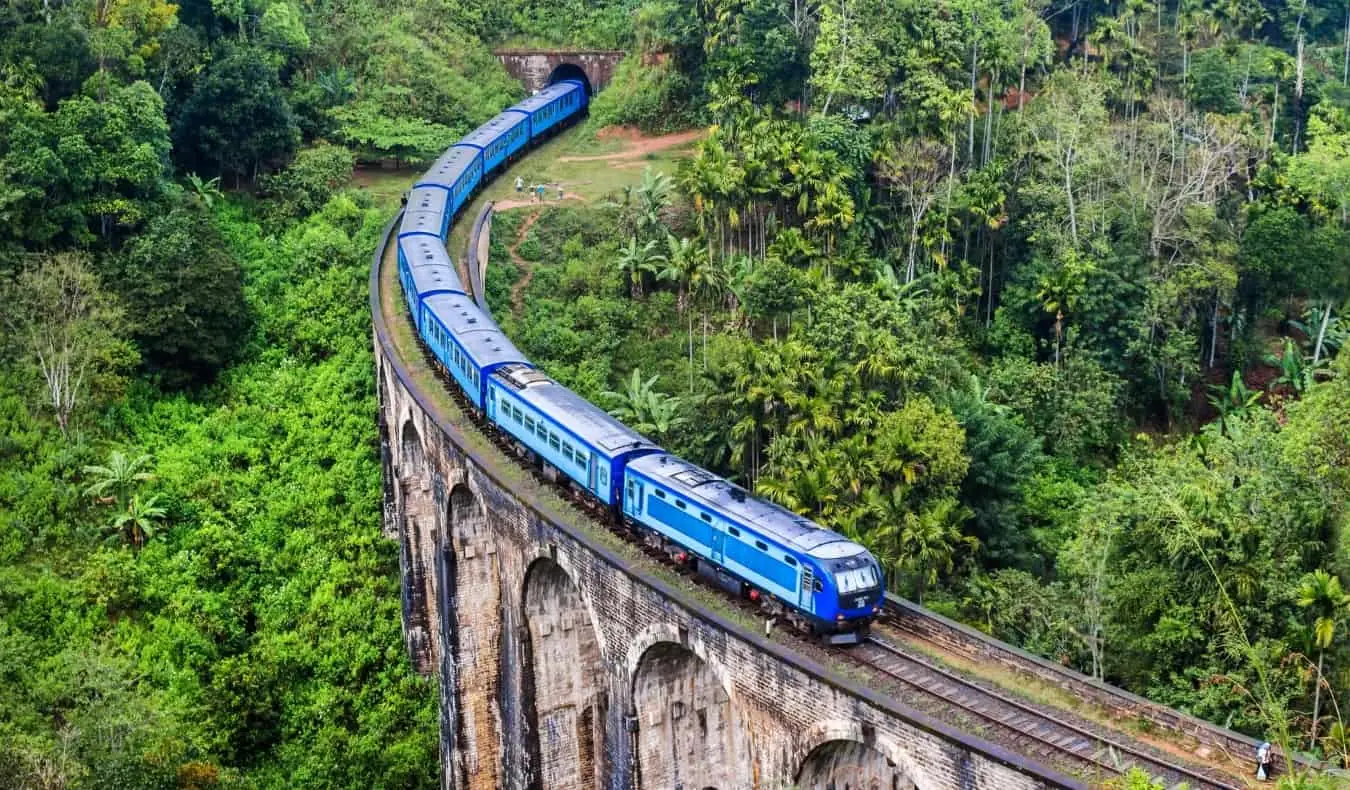 Un treno blu attraversa lo storico ponte a nove archi nello Sri Lanka, circondato da una giungla lussureggiante