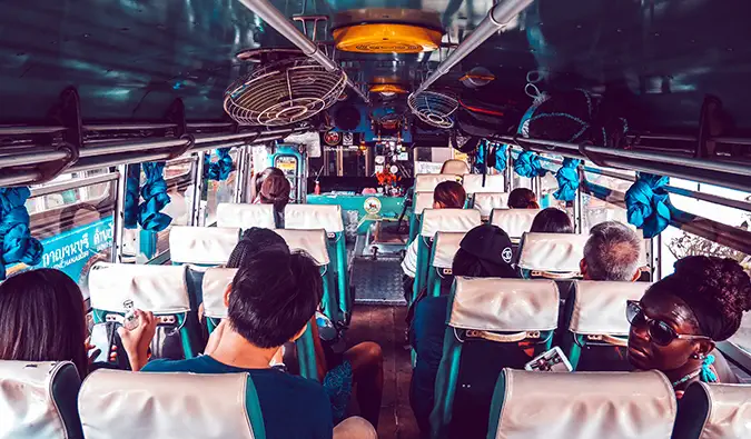 Menschen an Bord eines überfüllten Busses in Thailand mit an der Decke befestigten Ventilatoren