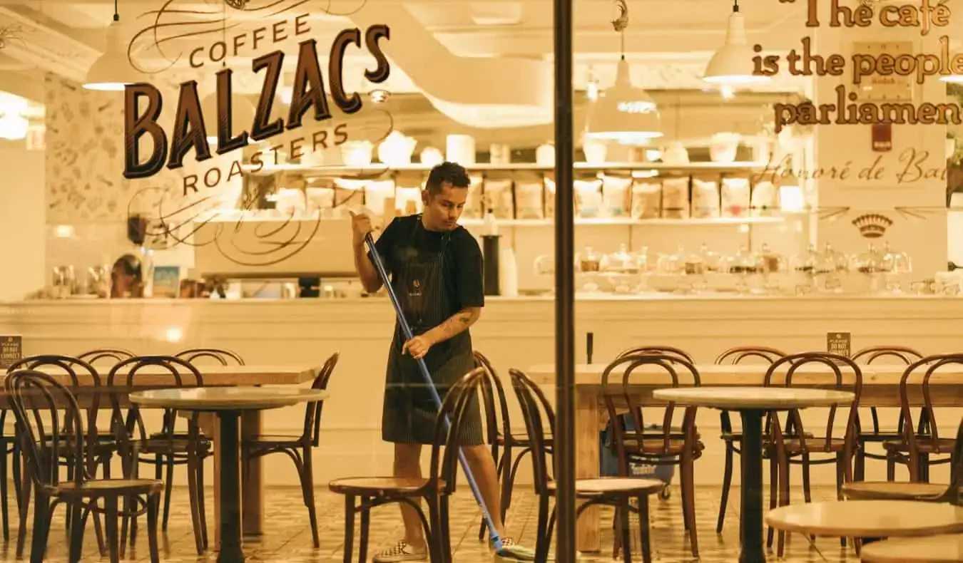 Ein junger männlicher Arbeiter wischt nachts den Boden in einem Café und Restaurant