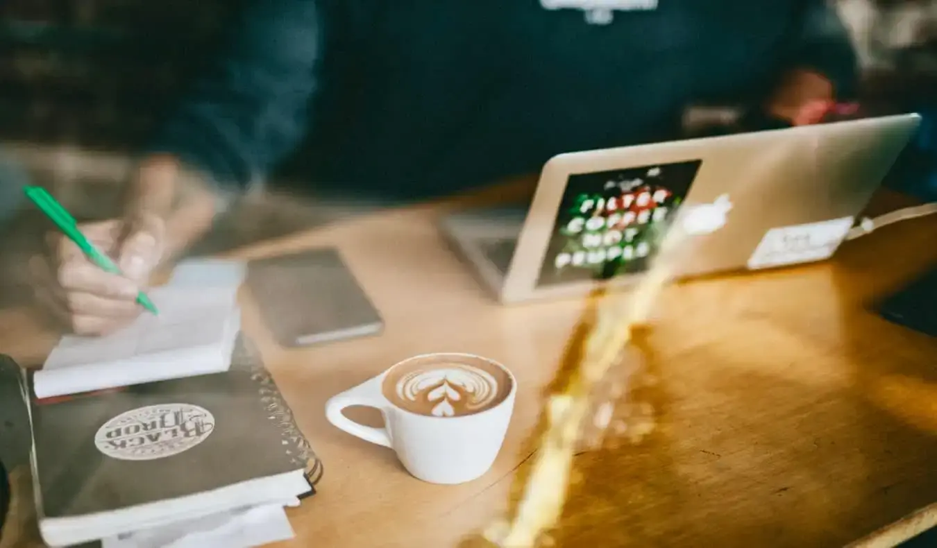 Ein Mann, der in einem Café online arbeitet und dabei einen Latte trinkt