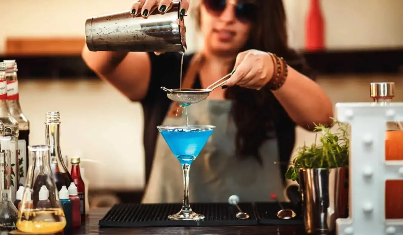 Una barista versa una bevanda colorata al bar