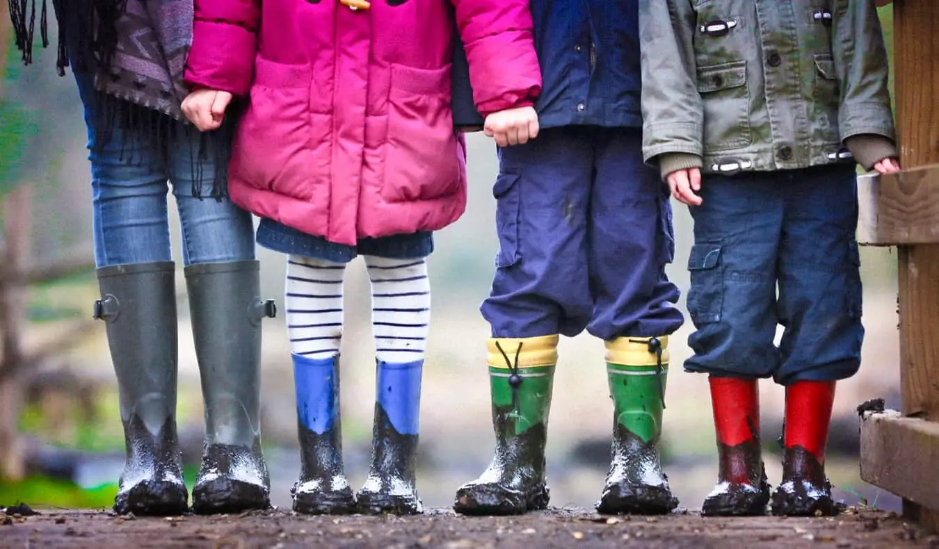 Ein Au-pair steht mit Kindern in Gummistiefeln im Schlamm