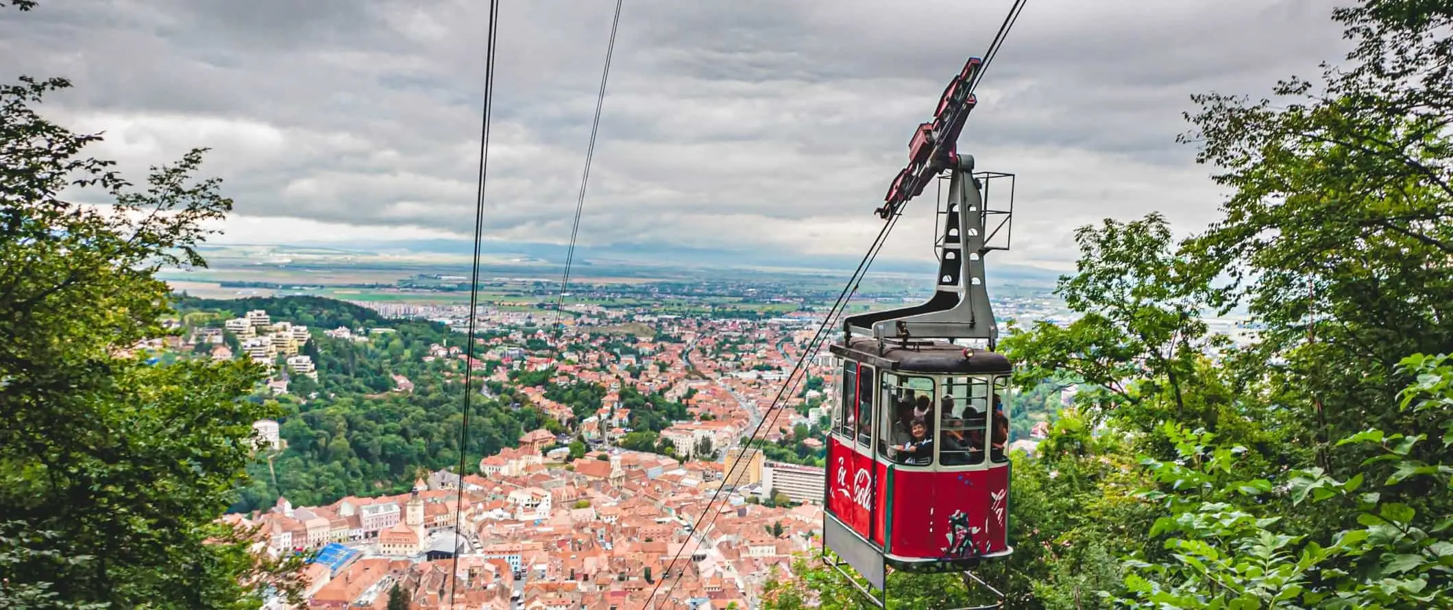 Svævebane går op ad bjerget med den gamle bydel i Brasov, Rumænien i baggrunden.