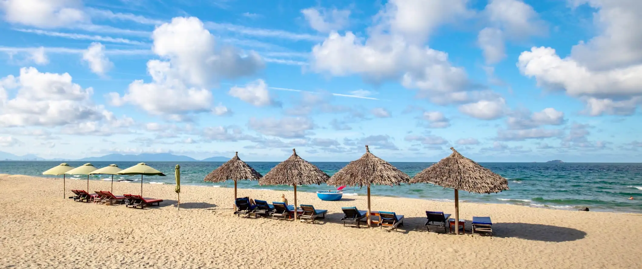 A gyönyörű strand székekkel és napernyőkkel a napsütötte Hoi An közelében, Vietnamban