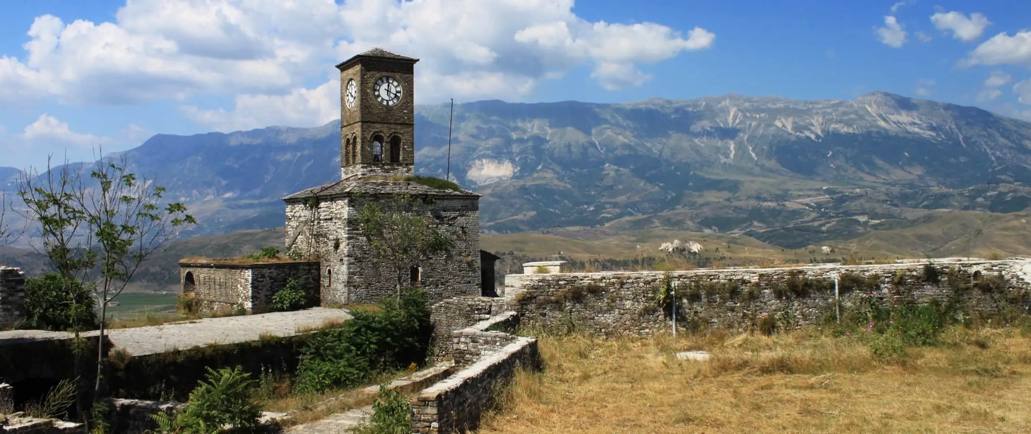 Une vieille tour en pierre et un mur de pierre en Albanie avec des collines et des montagnes au loin