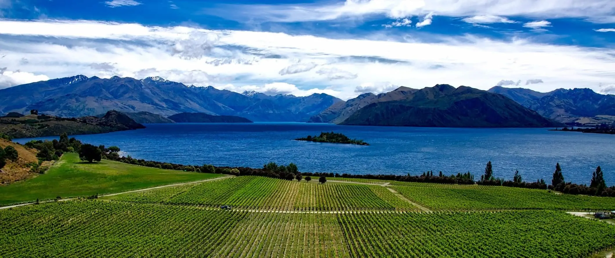 Roys Peak, un munte celebru în prim plan, cu munți și lacuri în spate în Wanaka, Noua Zeelandă.