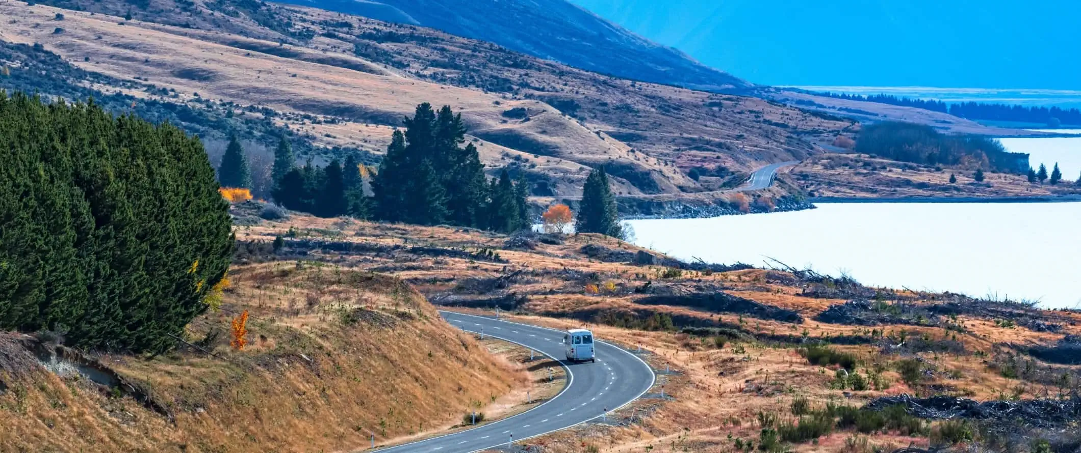 Furgoneta care conduce pe un drum întortocheat de-a lungul unui lac lângă Wanaka, Noua Zeelandă