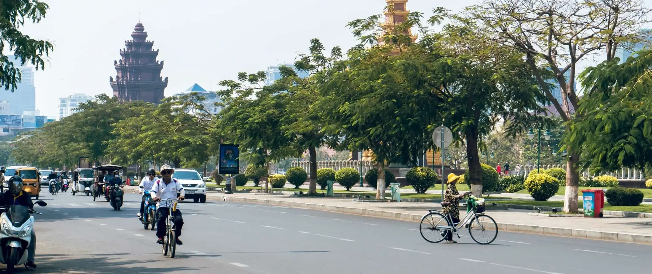 Mensen fietsen en motorrijden door een brede straat in Phnom Penh, Cambodja