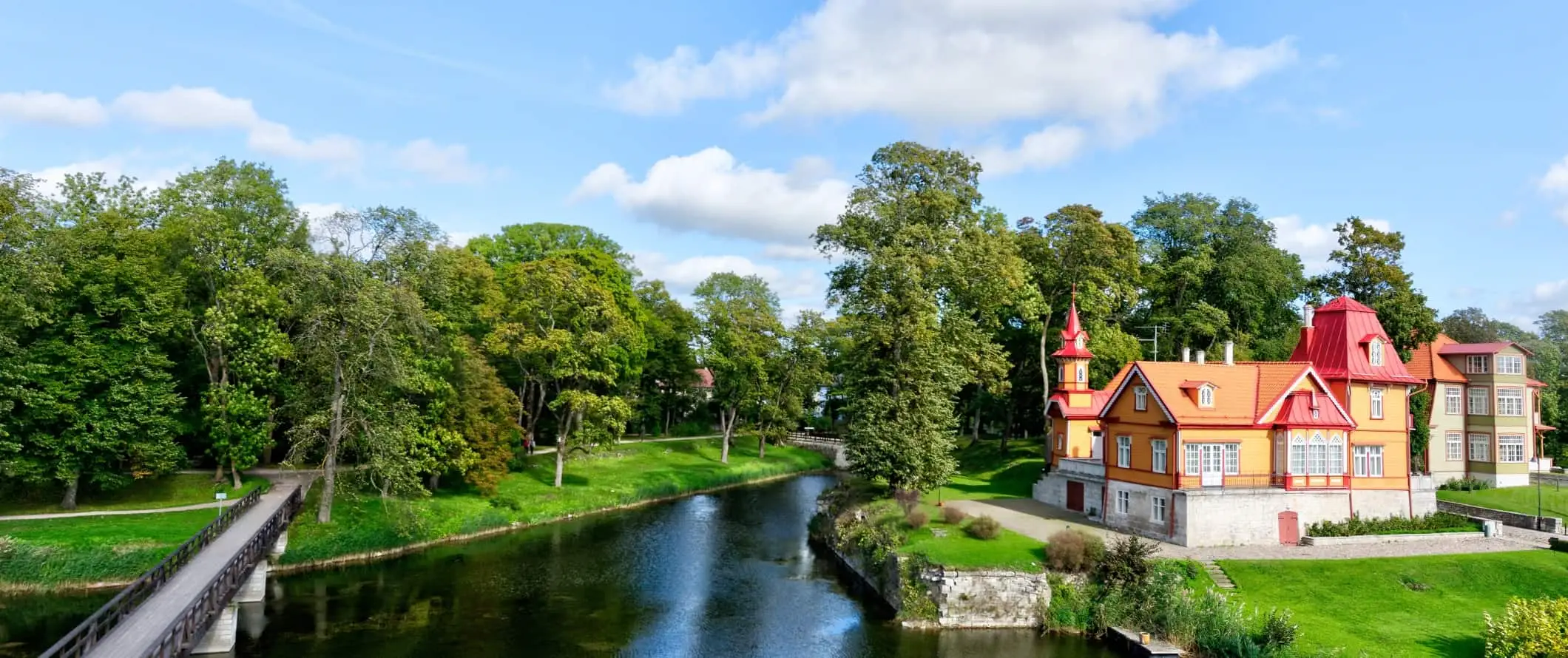 Matingkad na kulay na gusali sa kahabaan ng tree-lineed canal sa kanayunan ng Estonia