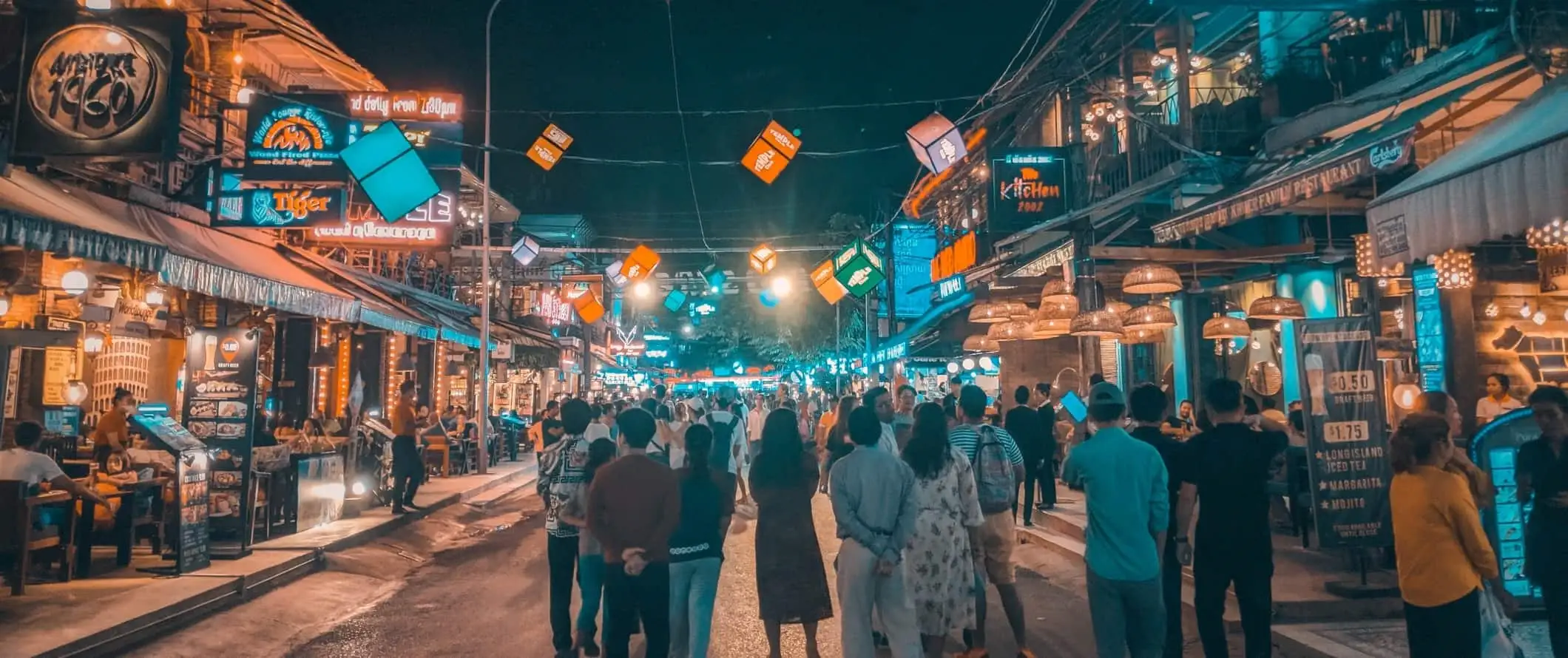 Orang ramai yang berjalan di jalan yang dipenuhi gerai makanan semuanya bercahaya pada waktu malam di Siem Reap, Kemboja