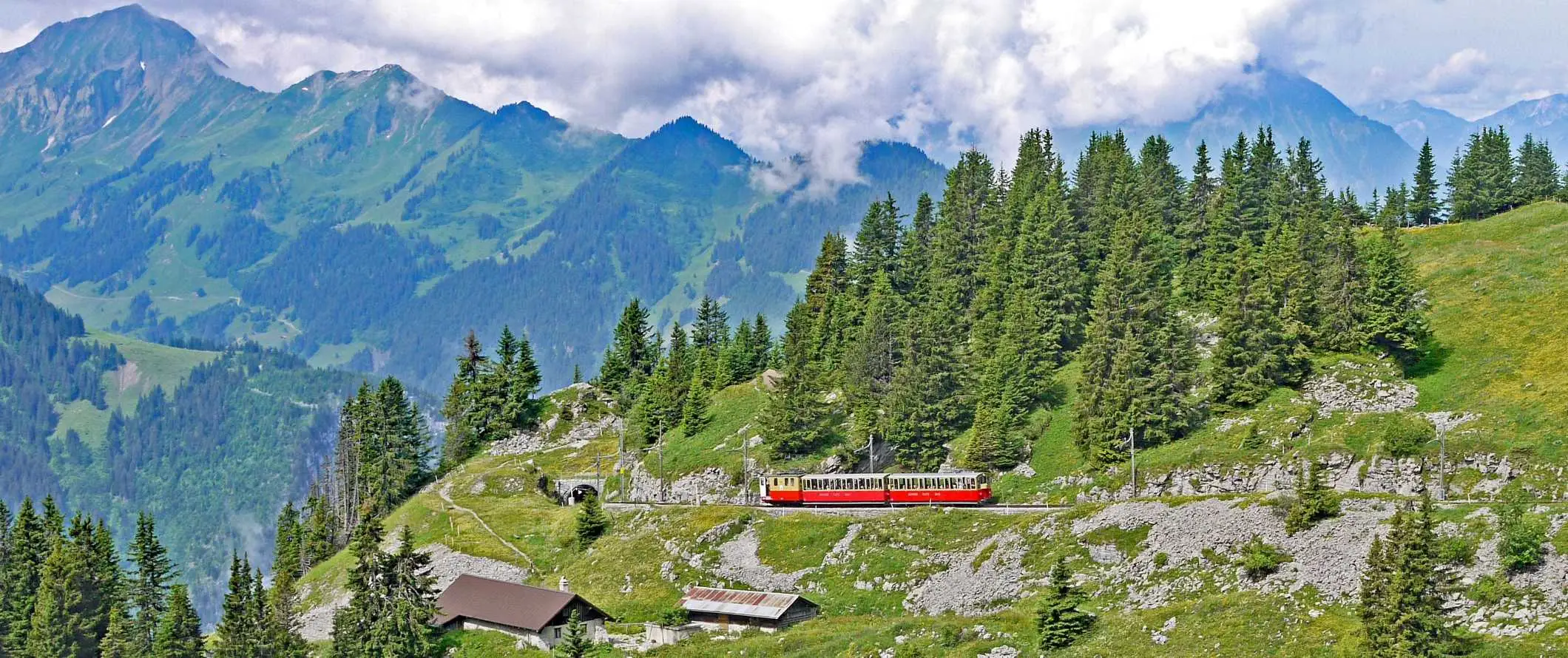 Červený vlak šplhající po dramatickém stoupání s ostrými horskými štíty v pozadí na železnici Jungfraujoch v Interlaken, Švýcarsko