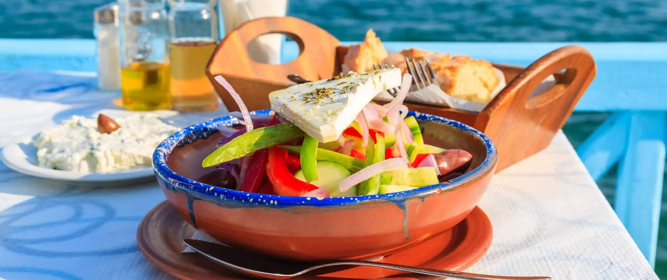 Griekse salade, olijfolie, brood en dipsaus aan een tafel aan de oceaan in Griekenland