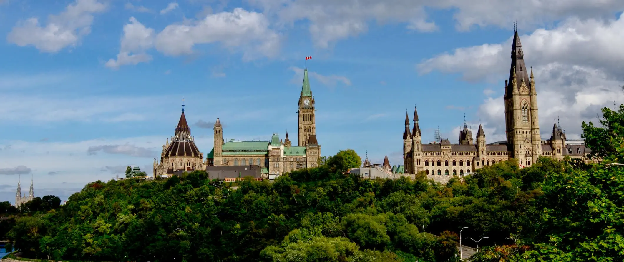 En utsikt over skyline av Ottawa, Canada, med parlamentsbygningene omgitt av frodige grønne trær om sommeren