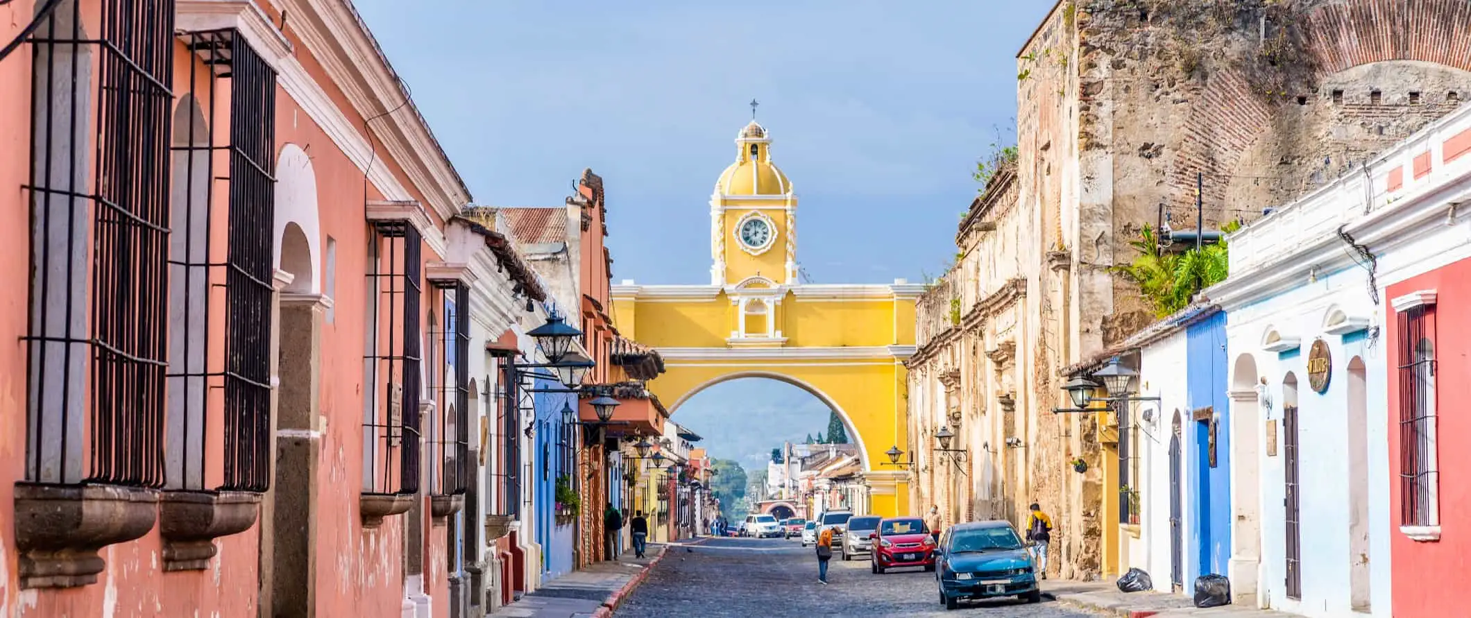 Von Kopfsteinpflaster gesäumte Straße mit bunten niedrigen Gebäuden auf beiden Seiten, mit einem gelben Torbogen, der über die Straße in Guatemala führt