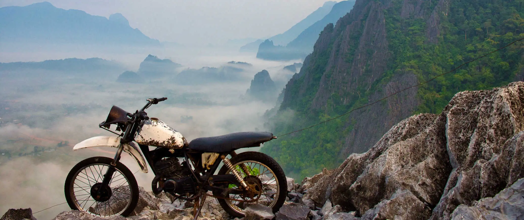 En gammel motorcykel parkeret på et bjerg med udsigt over landskabet nær Vang Vieng, Laos