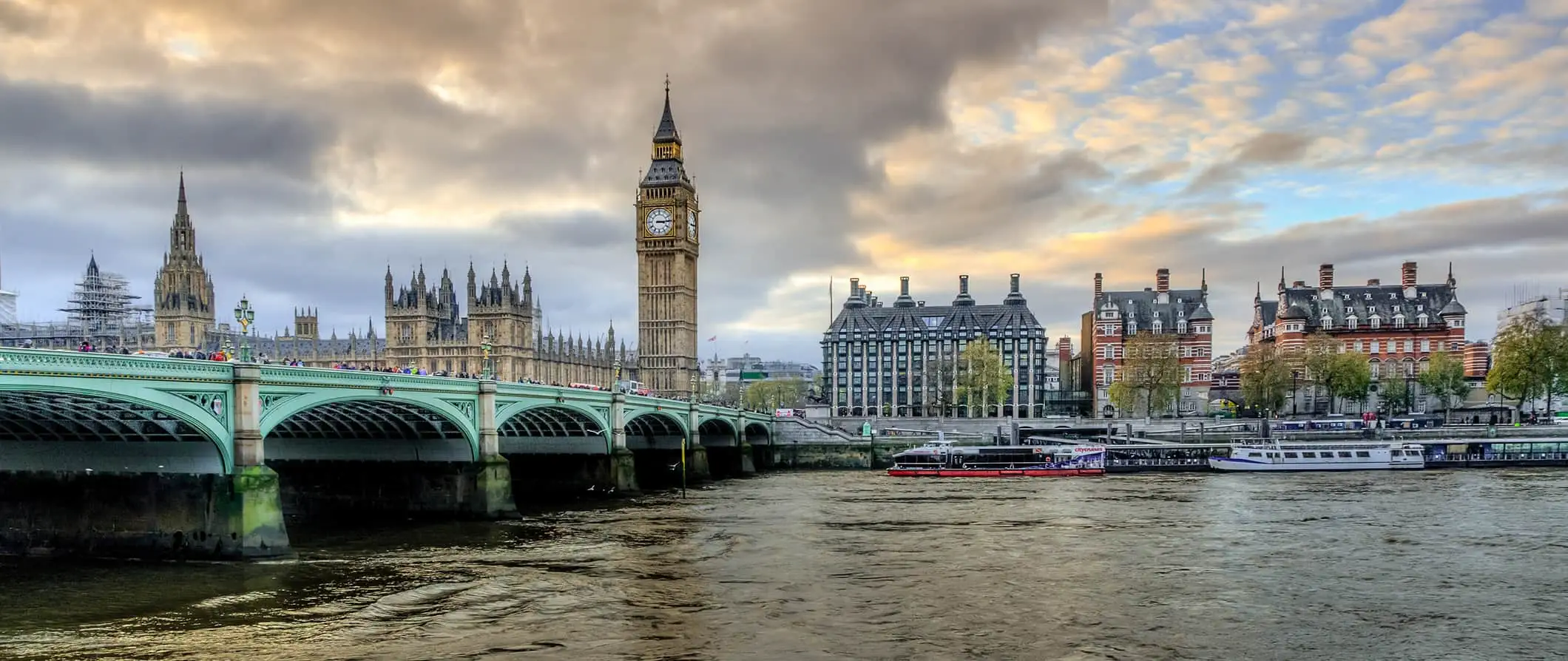 Uzaktaki tarihi binalar ve ön planda nehir ile Londra, İngiltere'de bulutlu bir günde ünlü Londra Köprüsü