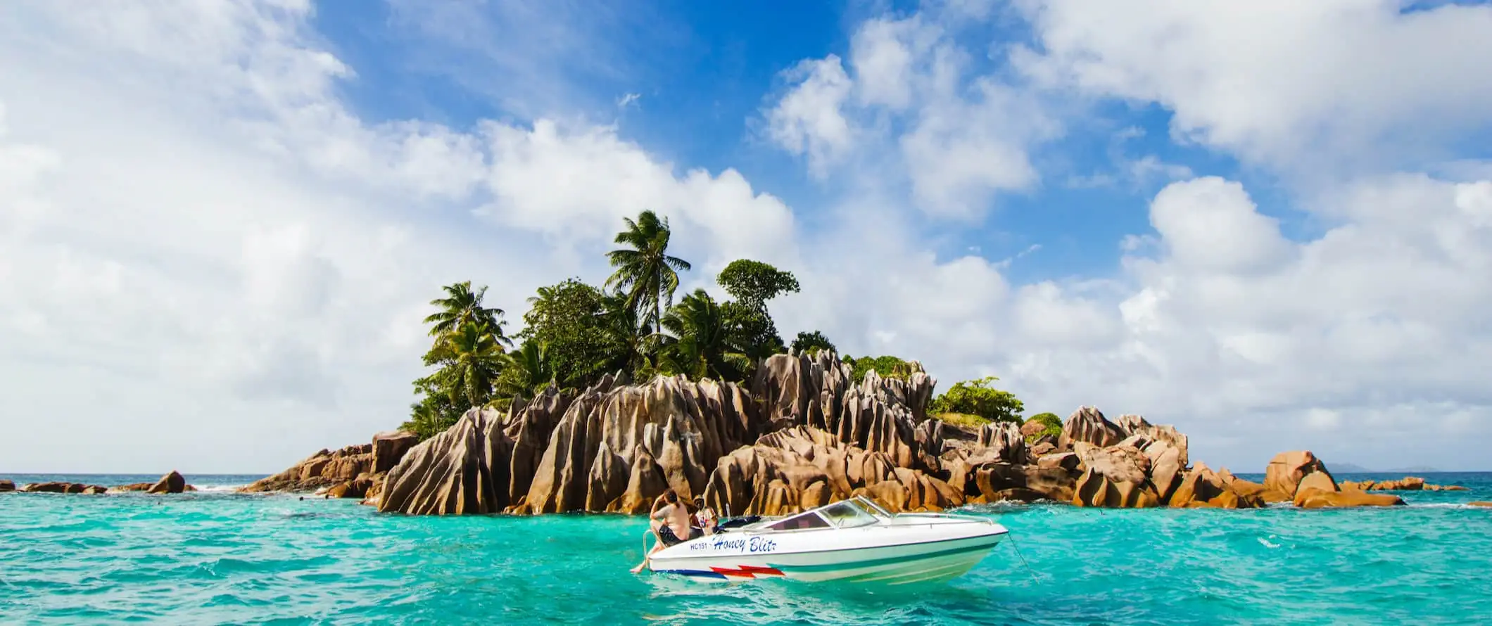 Sebuah bot berlabuh berhampiran sebuah pulau kecil di Seychelles semasa hari cerah yang indah