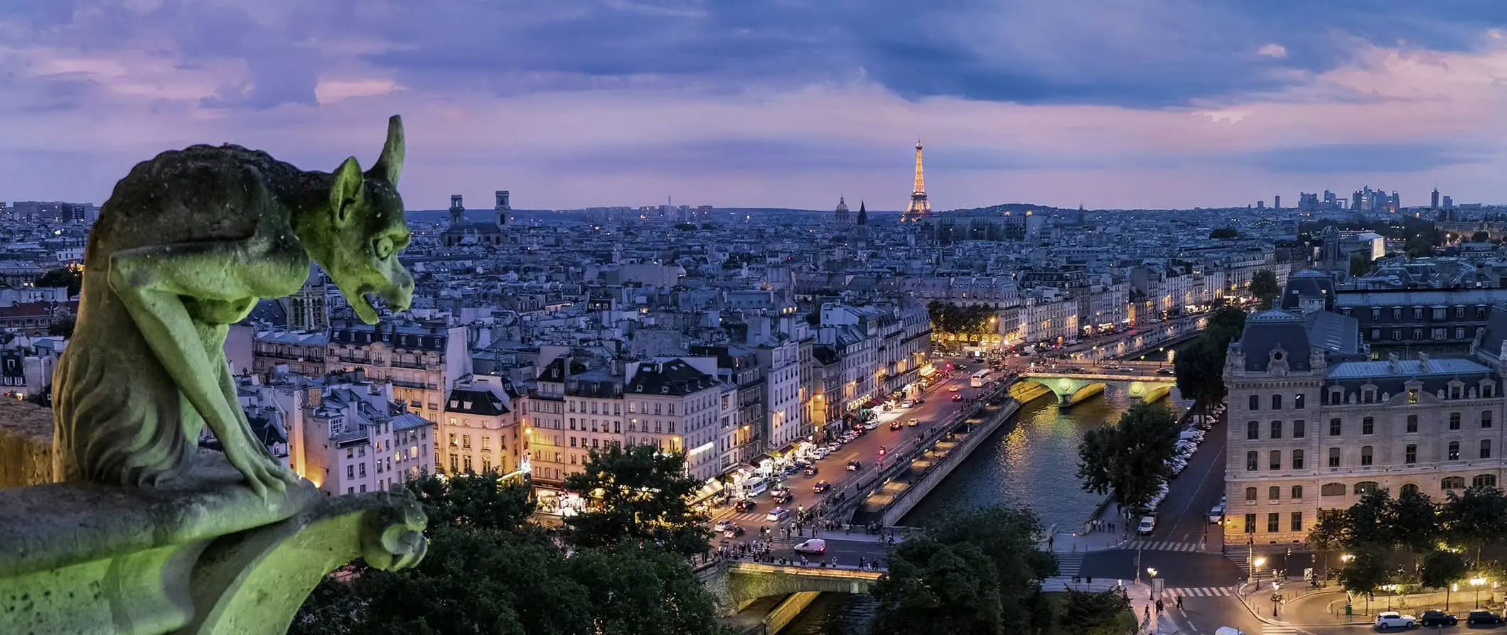 Şehrin silüeti üzerinde pembe bir gün batımı sırasında Paris'teki eski bir binanın ön planında bir çirkin yaratık