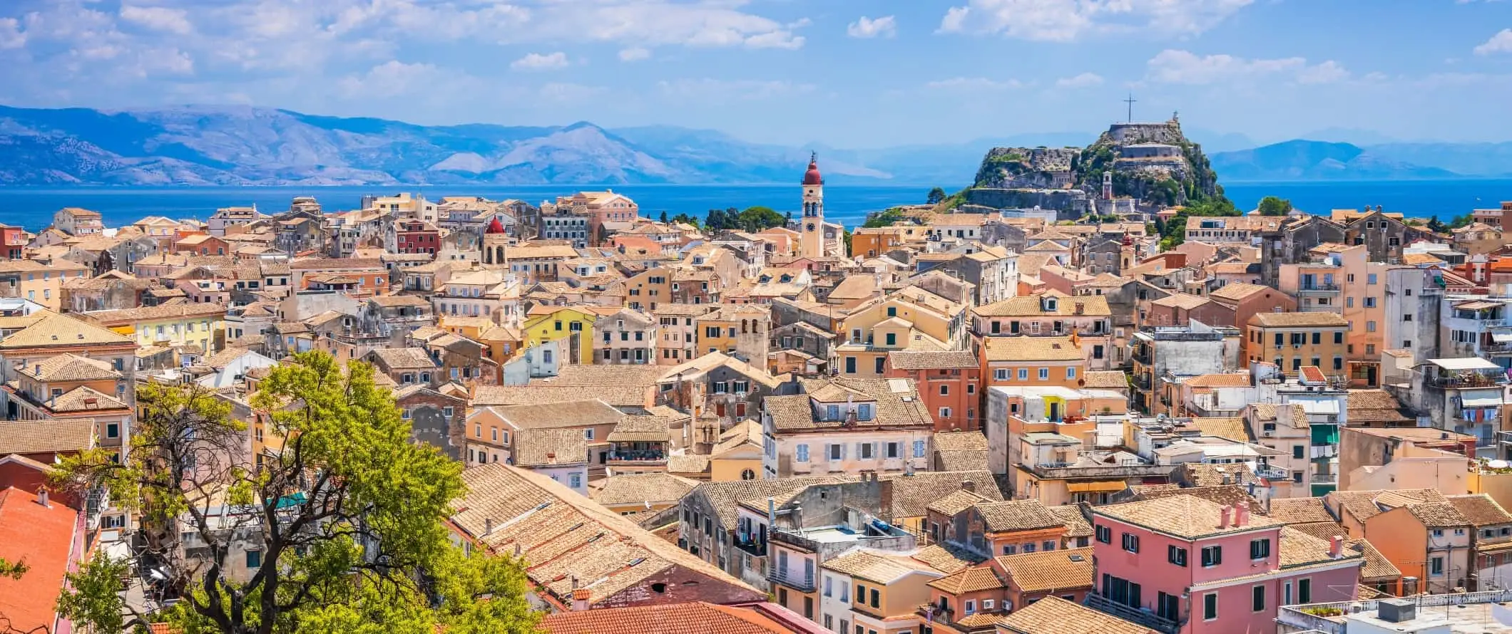 Vista aérea da cidade de Corfu em Corfu, Grécia, mostrando casas coloridas com telhados e oceanos e montanhas ao fundo.