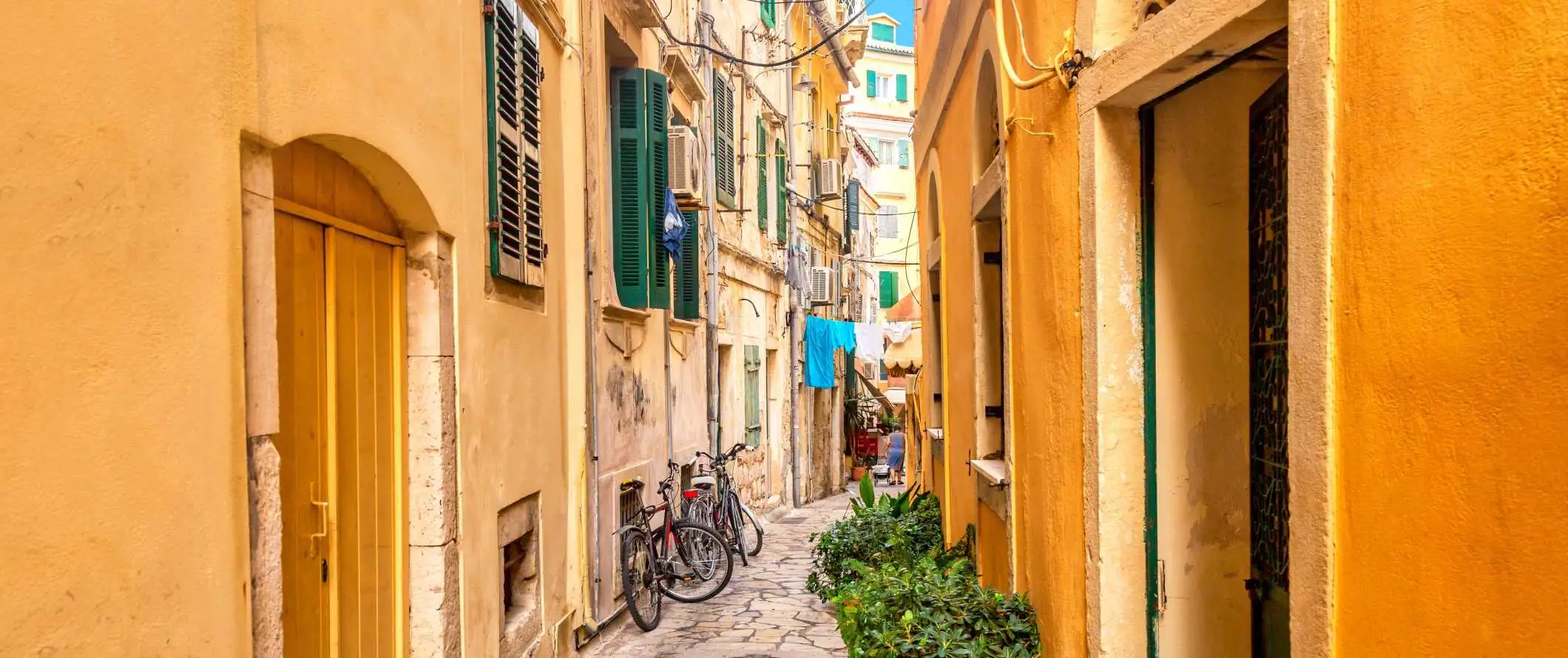 Petite rue dallée bordée de bâtiments jaune vif aux volets verts à Corfou, en Grèce.