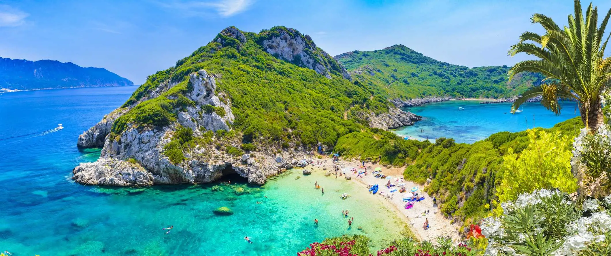 Pessoas descansando e nadando em uma praia com colinas exuberantes ao fundo e águas cristalinas e azul-turquesa em Corfu, Grécia