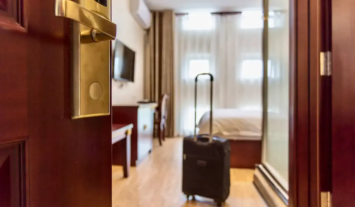 La porte d'une chambre d'hôtel confortable s'ouvre, avec une valise à roulettes à proximité