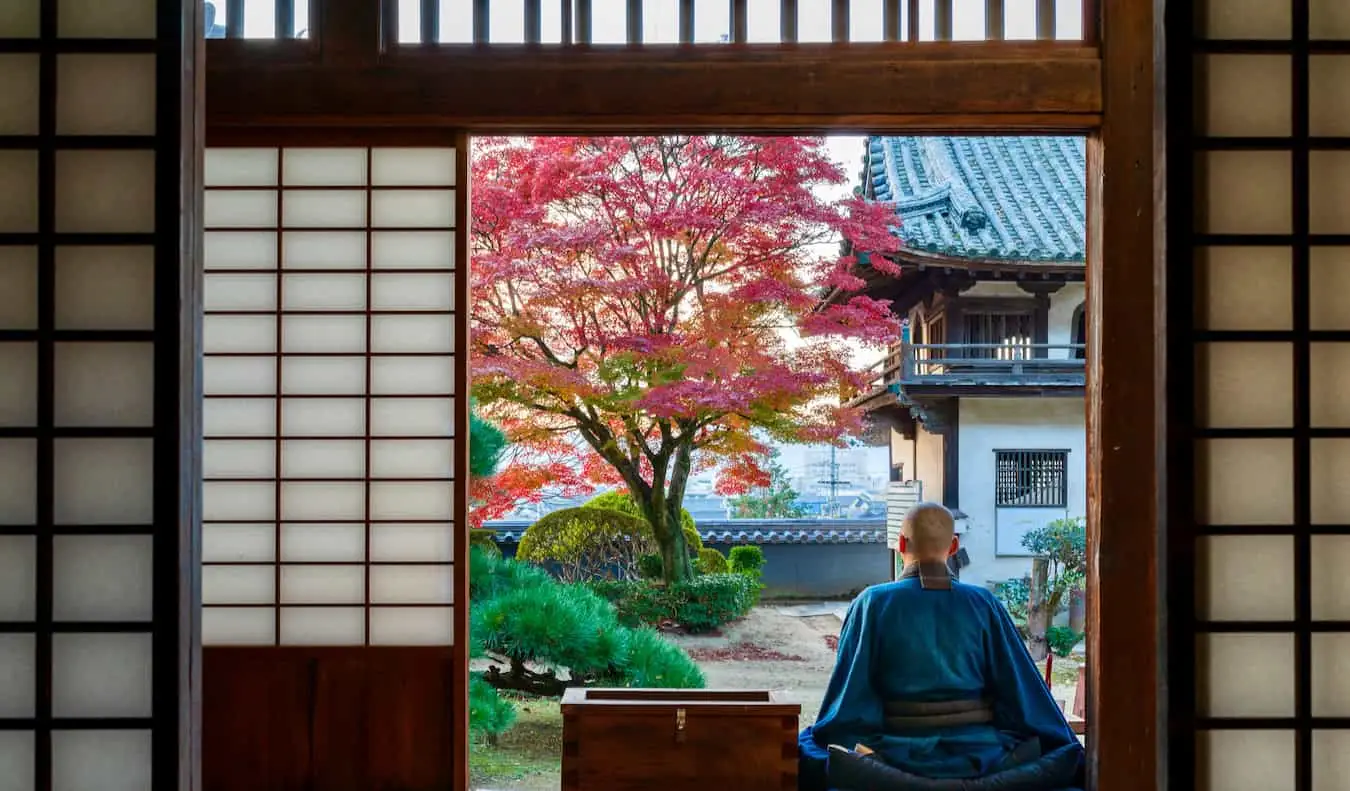 Un long moine bouddhiste assis sur le perron de son temple au Japon