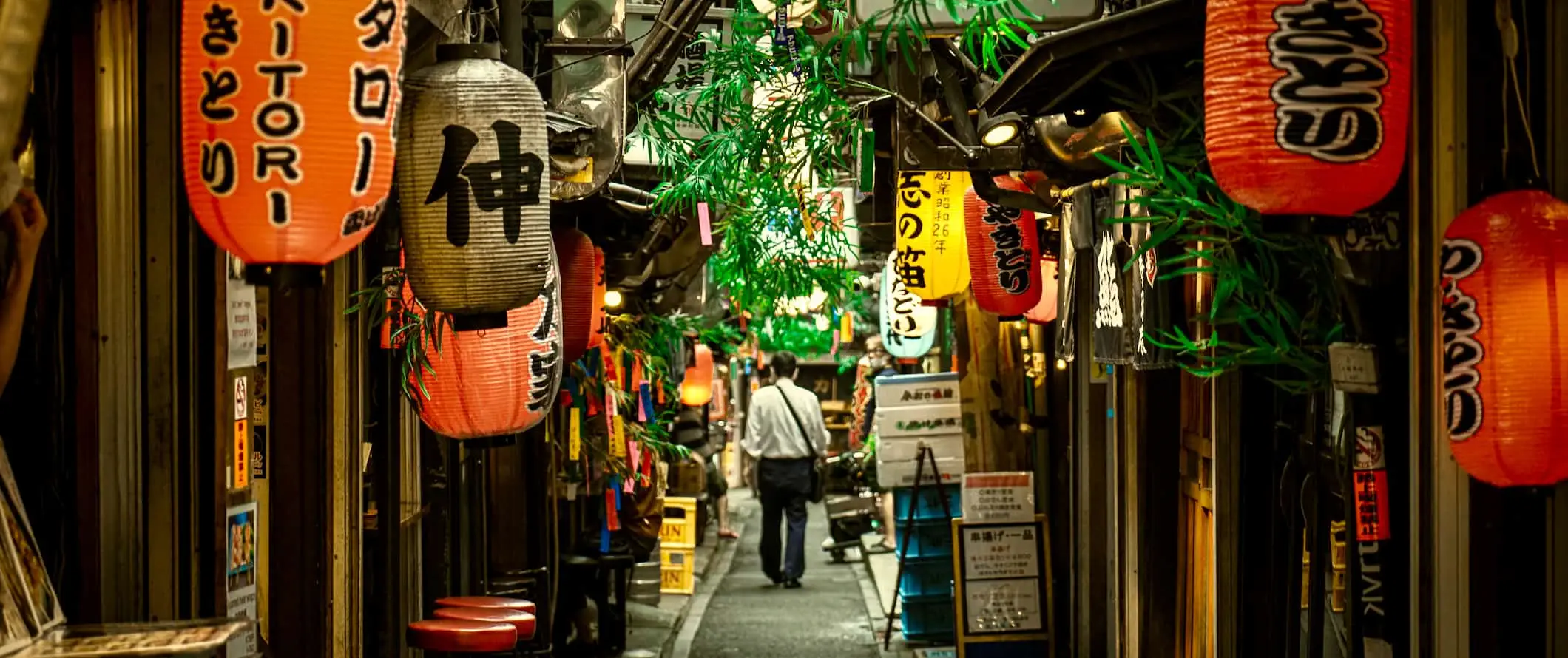 Un bărbat care merge pe o alee îngustă mărginită de magazine din Tokyo, Japonia