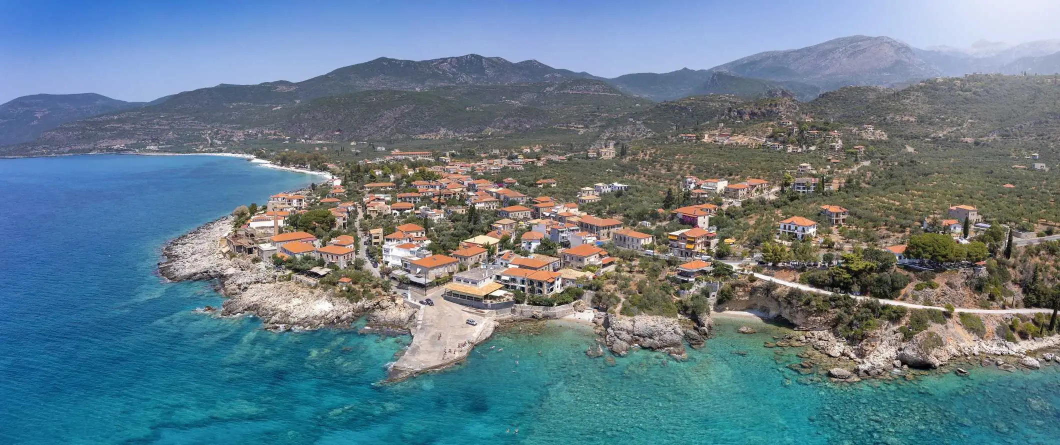 Aerial view ng Greek town sa kahabaan ng Mediterranean ocean, na may mga bundok sa background