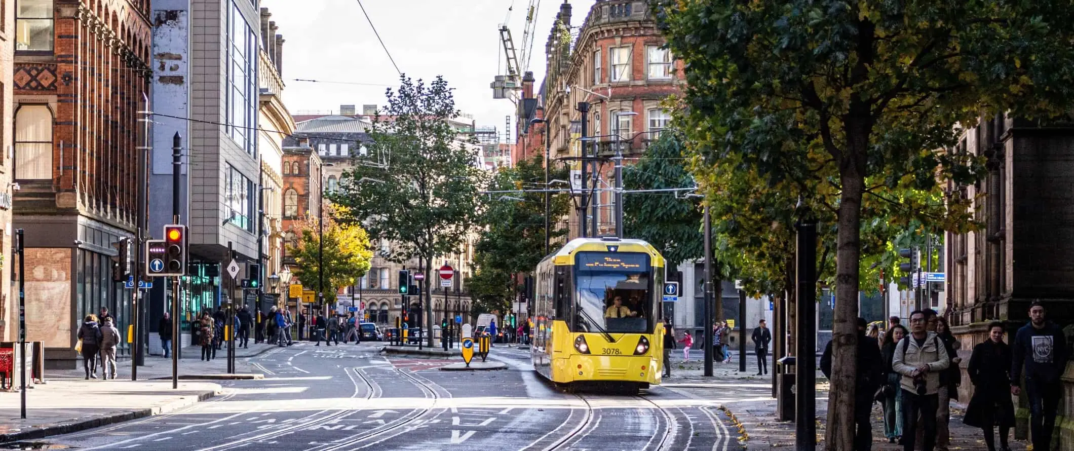 Pogled s ulice na ljude koji hodaju ulicom i žuti tramvaj koji prolazi u Manchesteru, Engleska