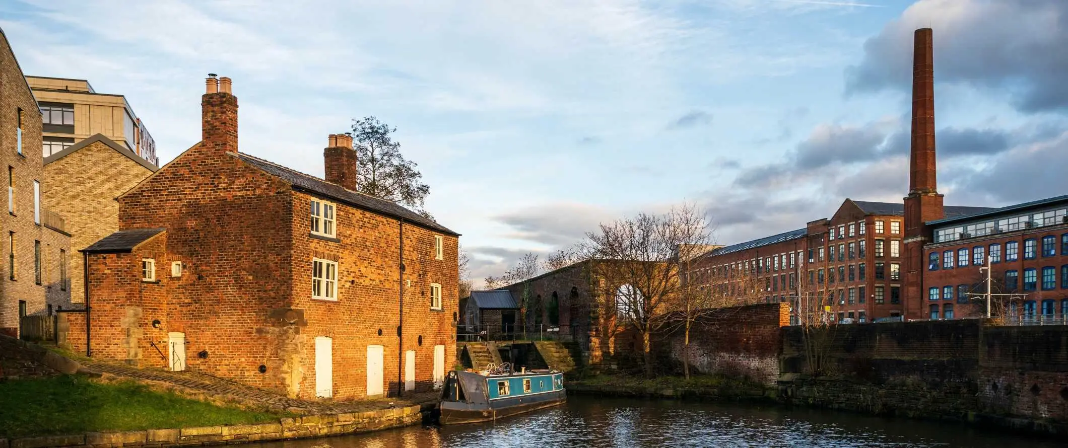 Historiske murbygninger og et lager langs en kanal med en liten båt i Manchester, England