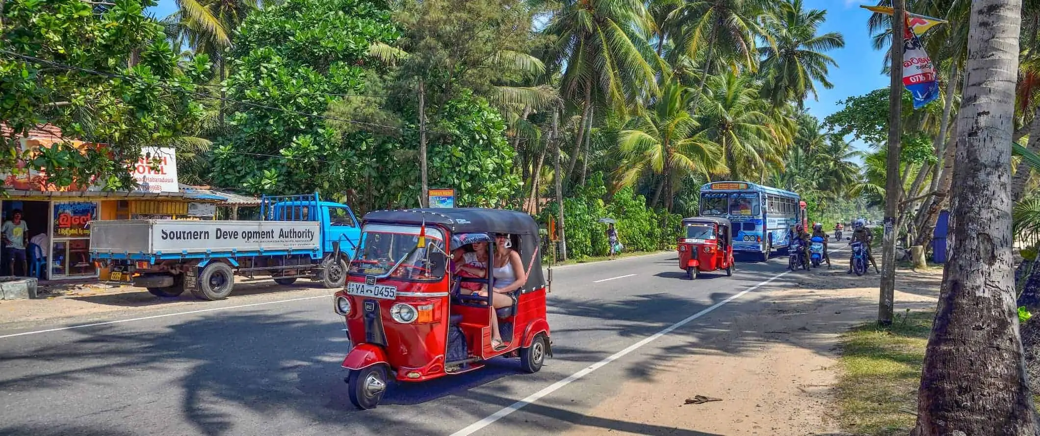 Tuk-tuky a autobusy na ceste lemovanej palmami na Srí Lanke