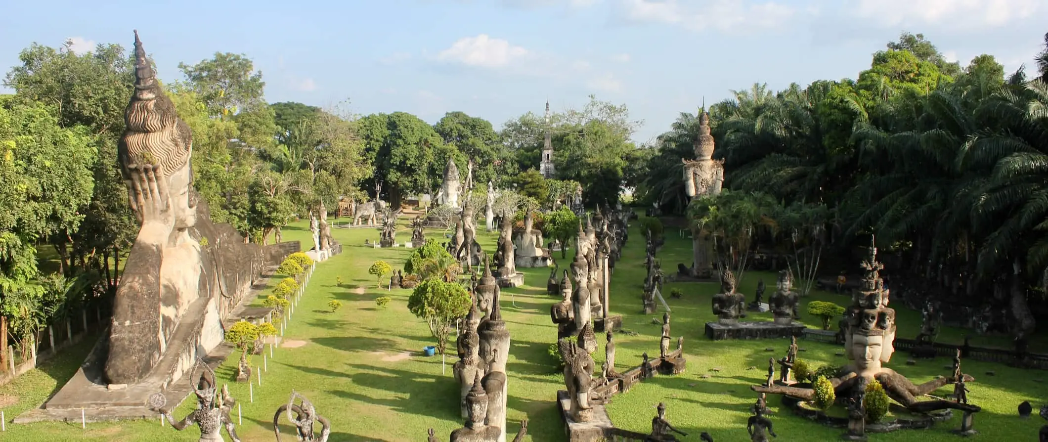 Dose-dosenang mga estadong Buddhist at Hindu sa Buddha Park malapit sa Vientiane, Laos na napapalibutan ng mga damo at puno