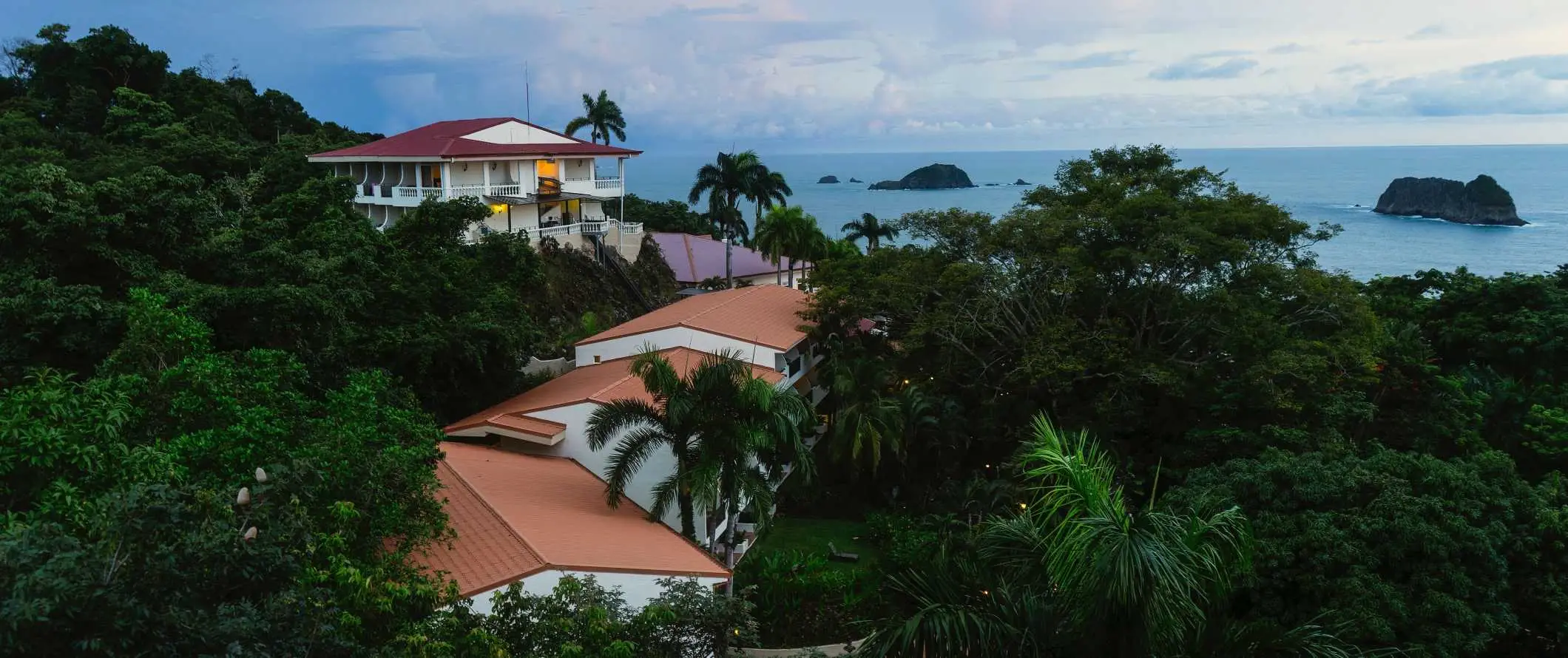 Kis üdülő- és szállodaépületek az esőerdőben, a háttérben az óceán Manuel Antonio-ban, Costa Rica-ban