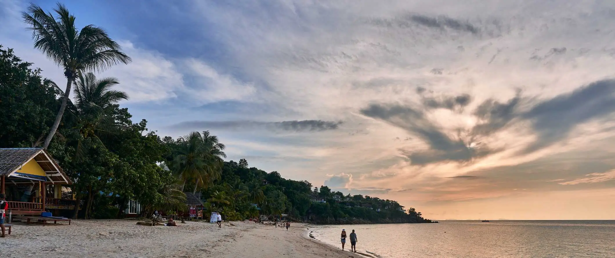 Menschen, die bei Sonnenuntergang am Strand auf der Insel Ko Pha Ngan, Thailand, bei Sonnenuntergang über dem Meer spazieren gehen