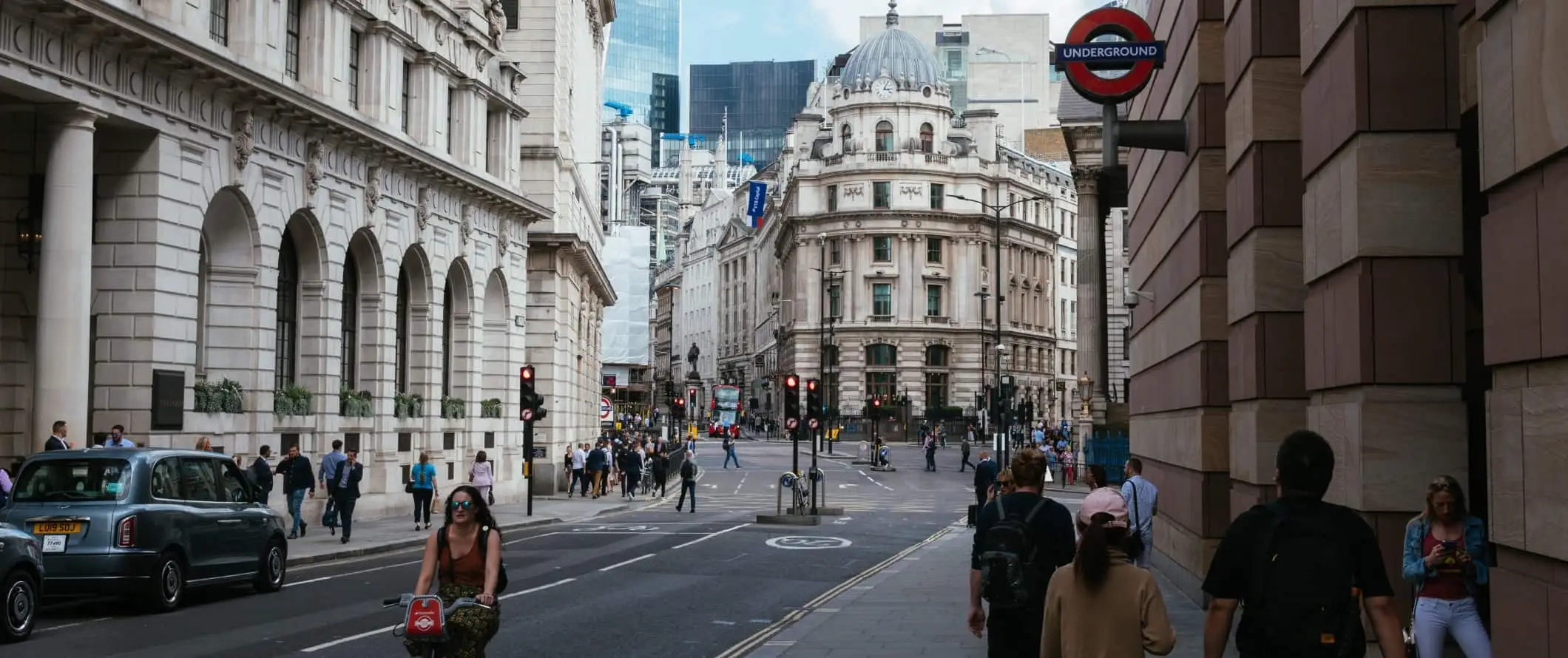 Gatebilde med folk som går rundt under et skilt for undergrunnen i London, England