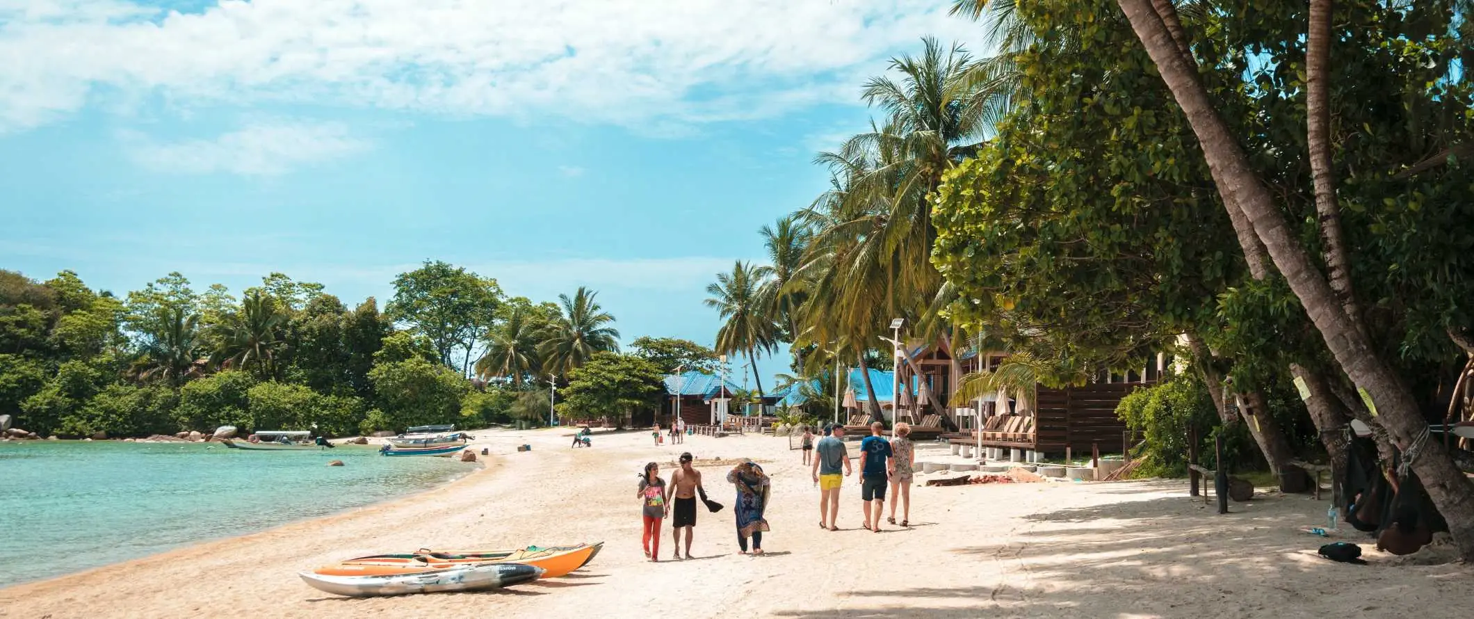 Žmonės vaikšto paplūdimiu su skaidriu vandeniu ir vešliomis palmėmis Perhentian salose, Malaizijoje