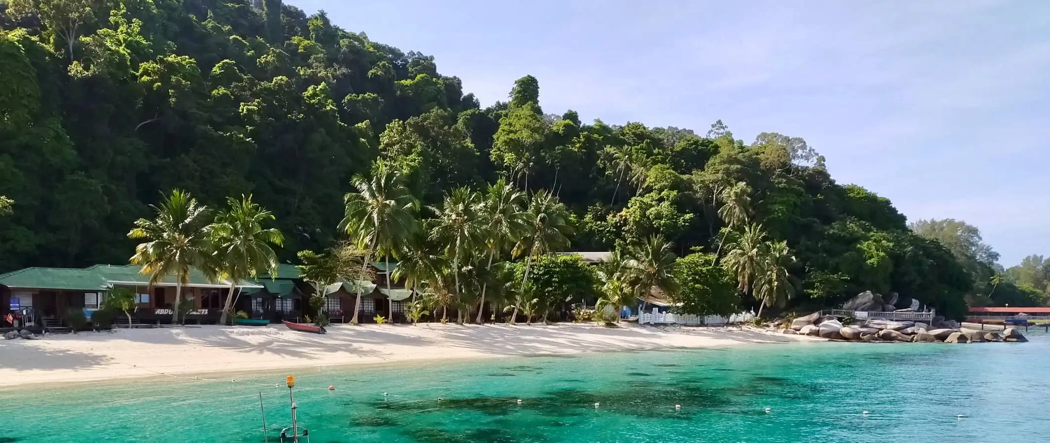 Isang nakamamanghang tanawin ng beach sa Perhentian Islands, Malaysia na may malinaw na tubig at malalagong mga palm tree at gubat