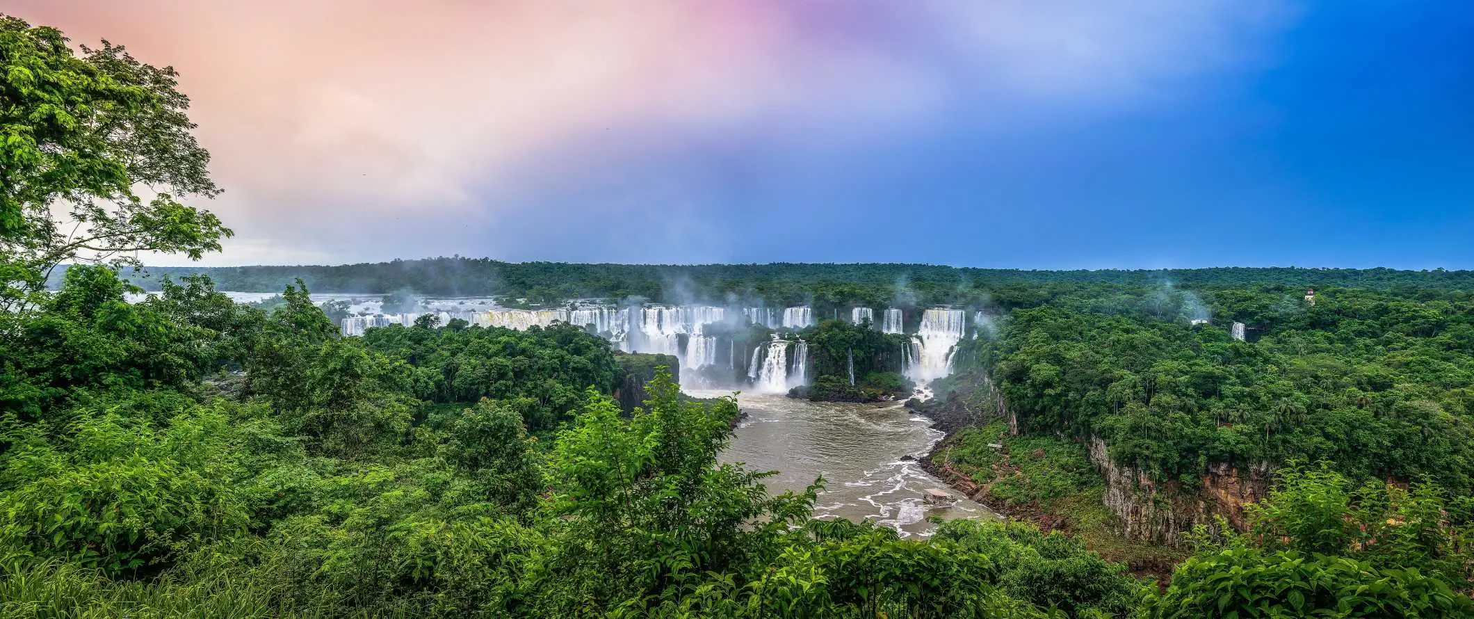 Οι εκτεταμένοι καταρράκτες Iguazu στη Βραζιλία μέσα στο καταπράσινο τροπικό δάσος το ηλιοβασίλεμα