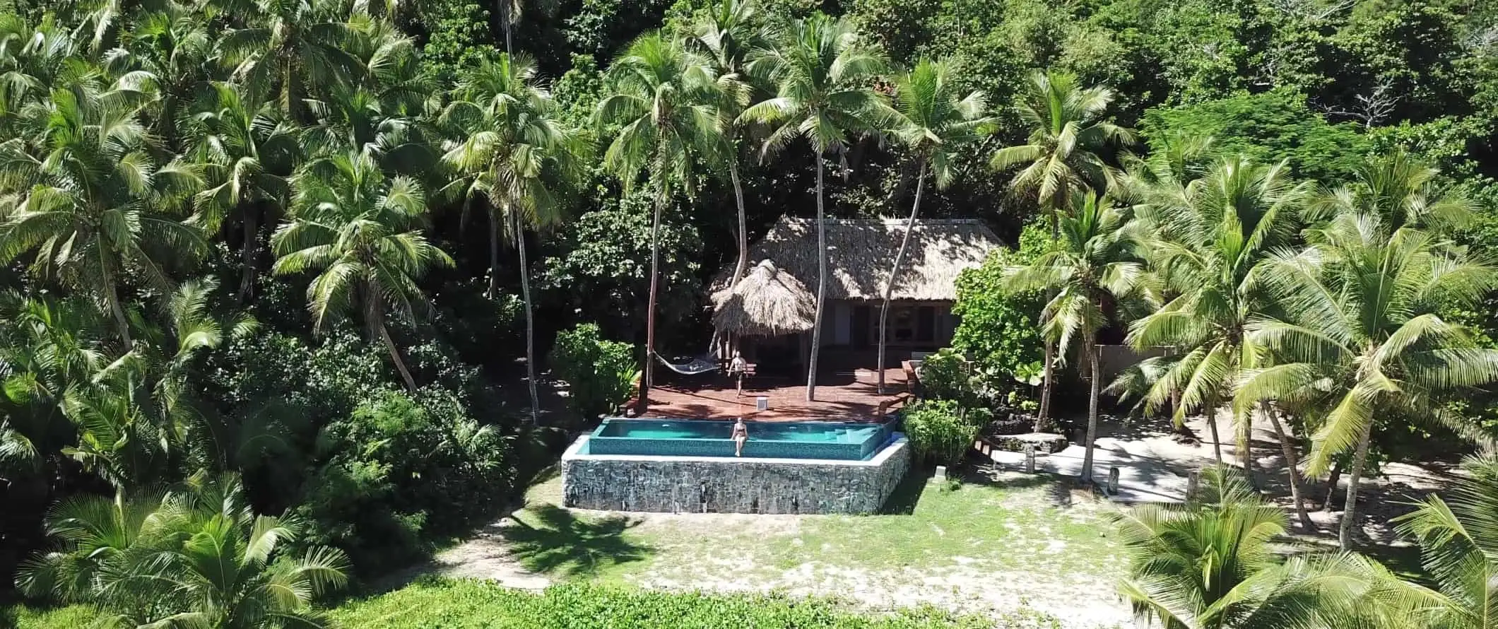 Orang yang duduk di kolam renang persendirian di hadapan pondok beratap jerami yang dikelilingi oleh pokok palma di Kepulauan Yasawa di Fiji