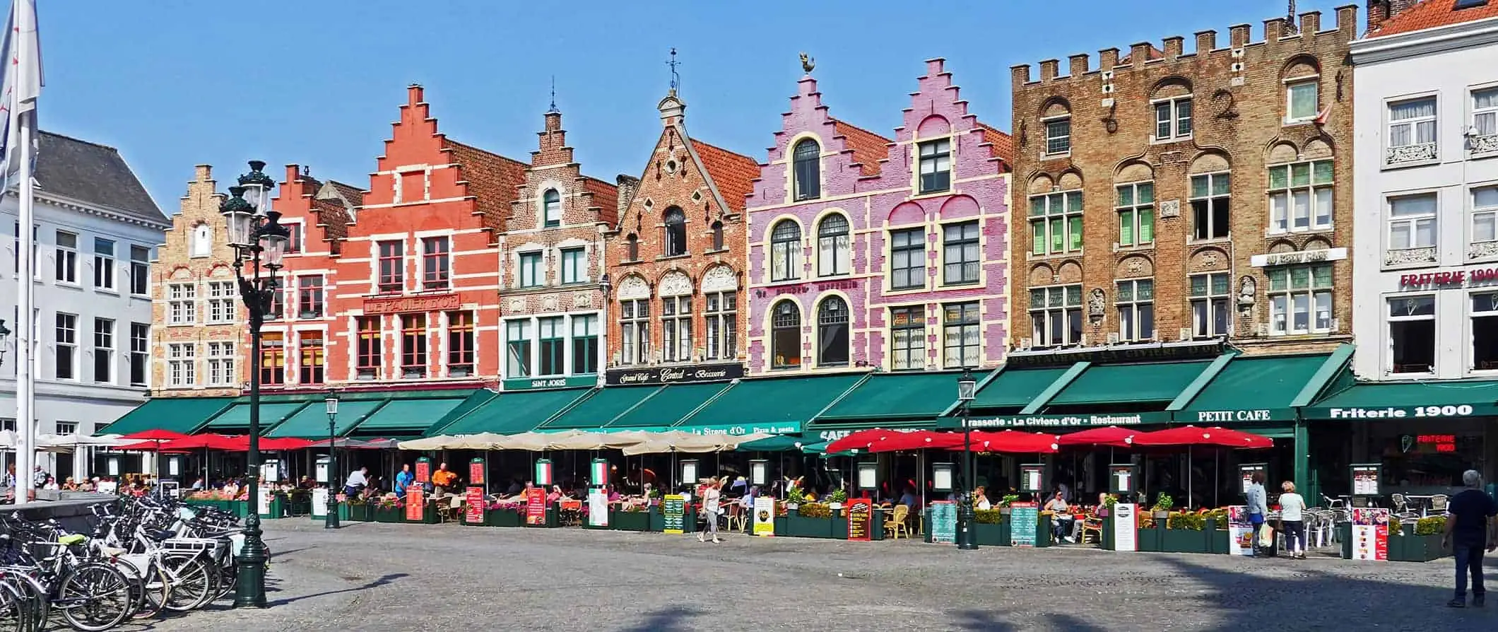 Eine farbenfrohe Straße mit alten Reihenhäusern in Brügge, Belgien, in der Nähe eines Platzes voller Menschen