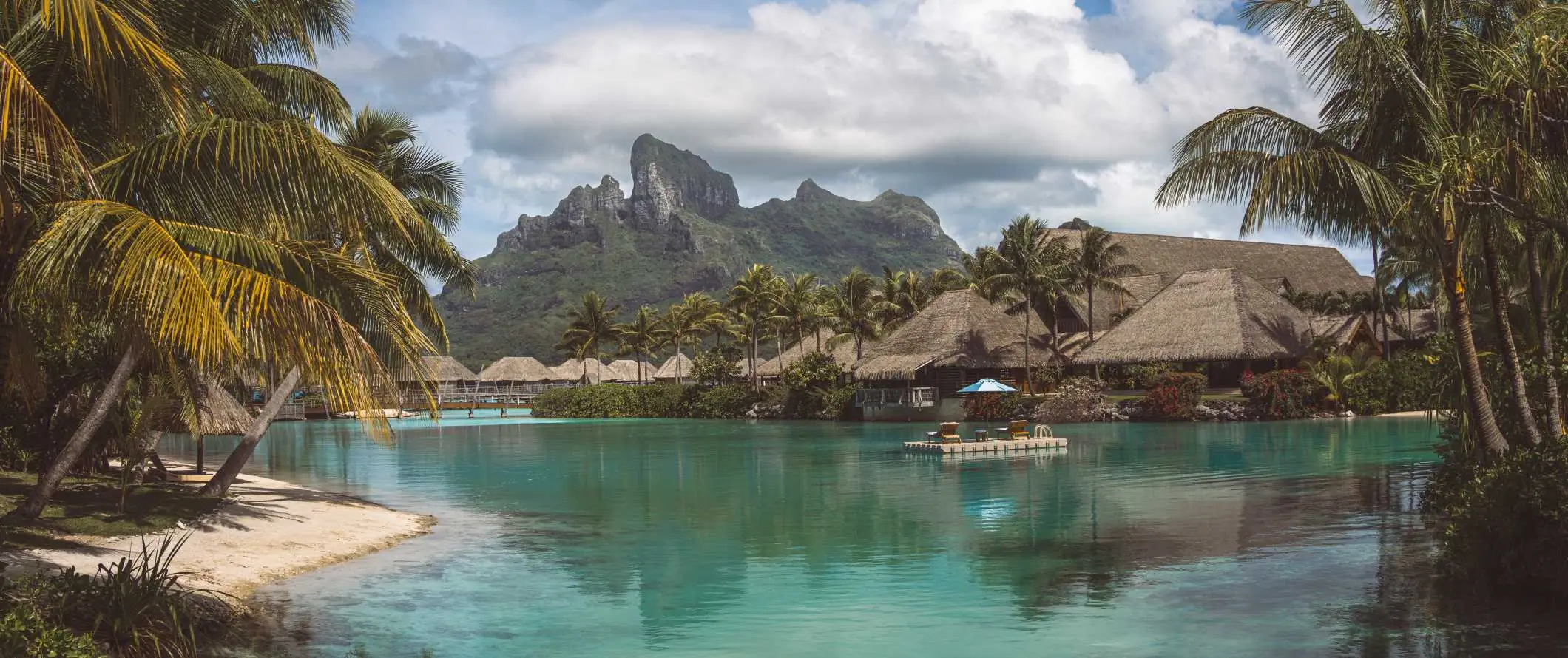 Overwater-Bungalows und klares Wasser mit einem scharfen Berggipfel im Hintergrund in Bora Bora, Französisch-Polynesien