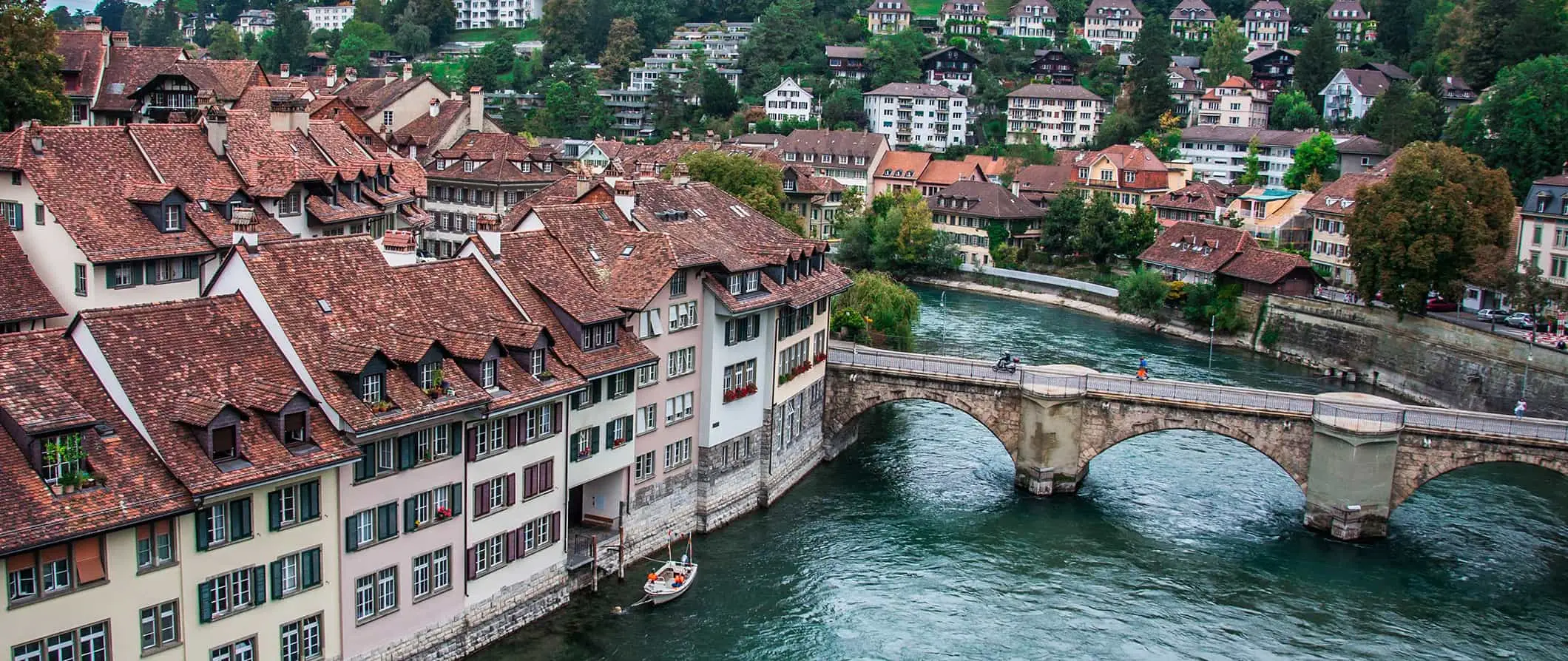 De charmerende bygninger i Bern, Schweiz langs floden med bjergskråningshuse i baggrunden