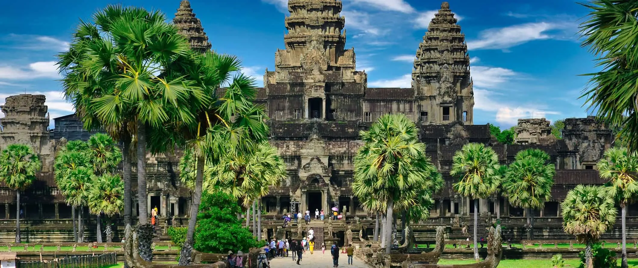 Besökare som går runt framför ett stort tempel omgivet av tropiska träd vid det historiska Angkor Wat-komplexet i Kambodja