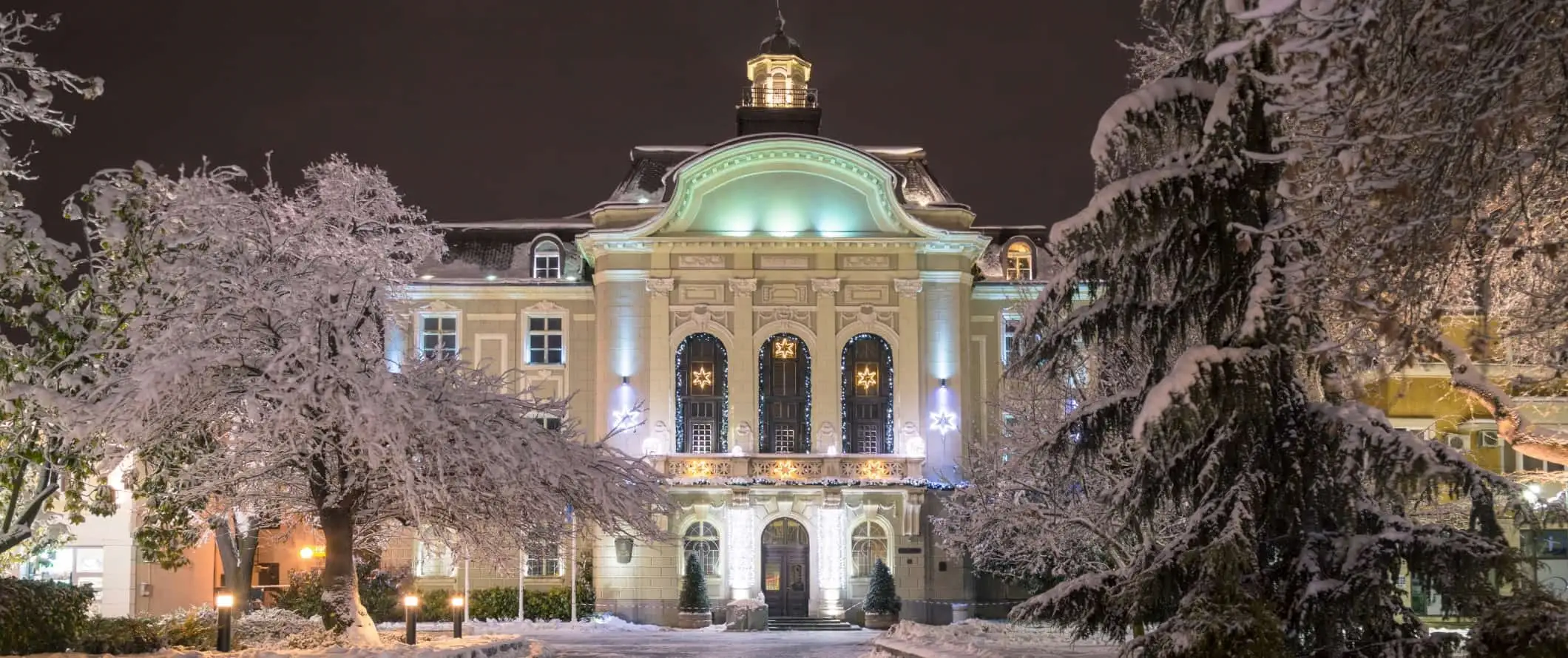 Un grande edificio storico circondato da alberi coperti di neve nella città vecchia di Plovdiv, Bulgaria