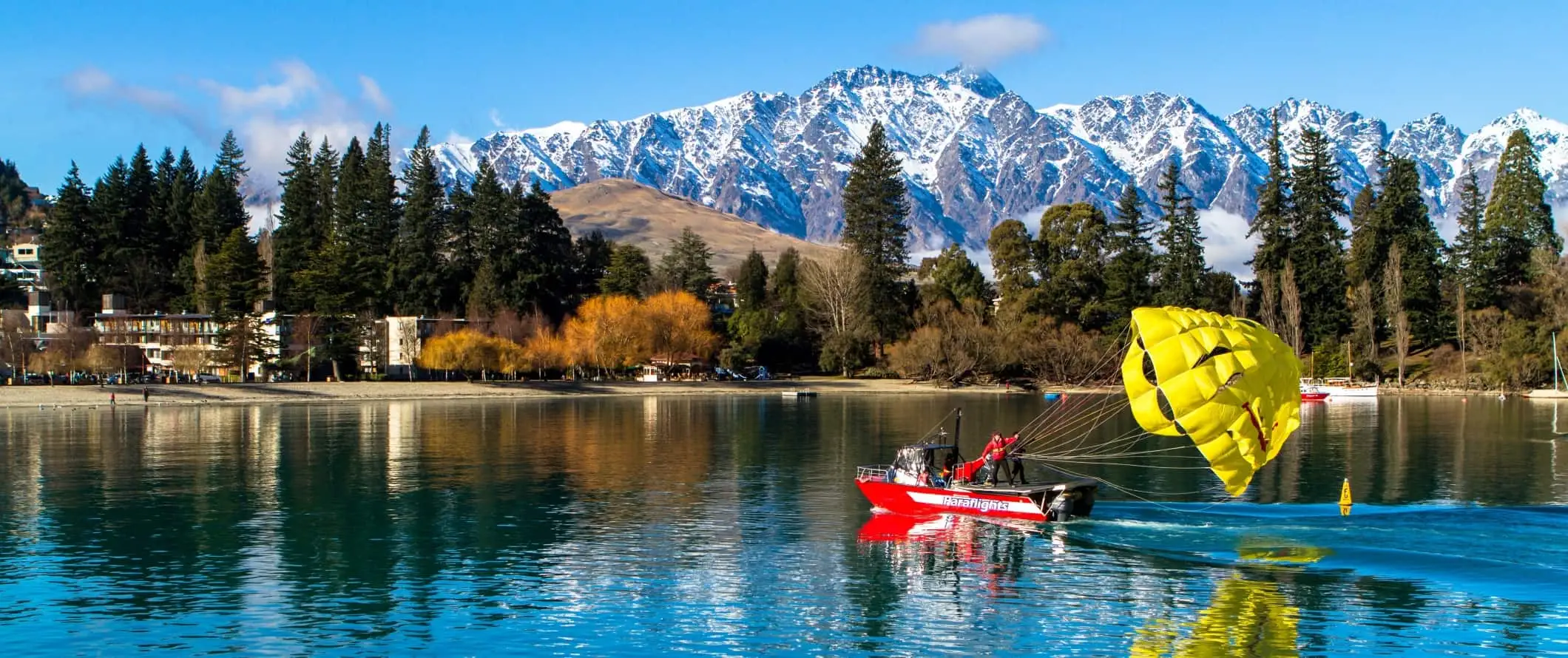 Vene, jonka takana on laskuvarjo Wakatipu-järvellä, Queenstownissa, Uudessa-Seelannissa.