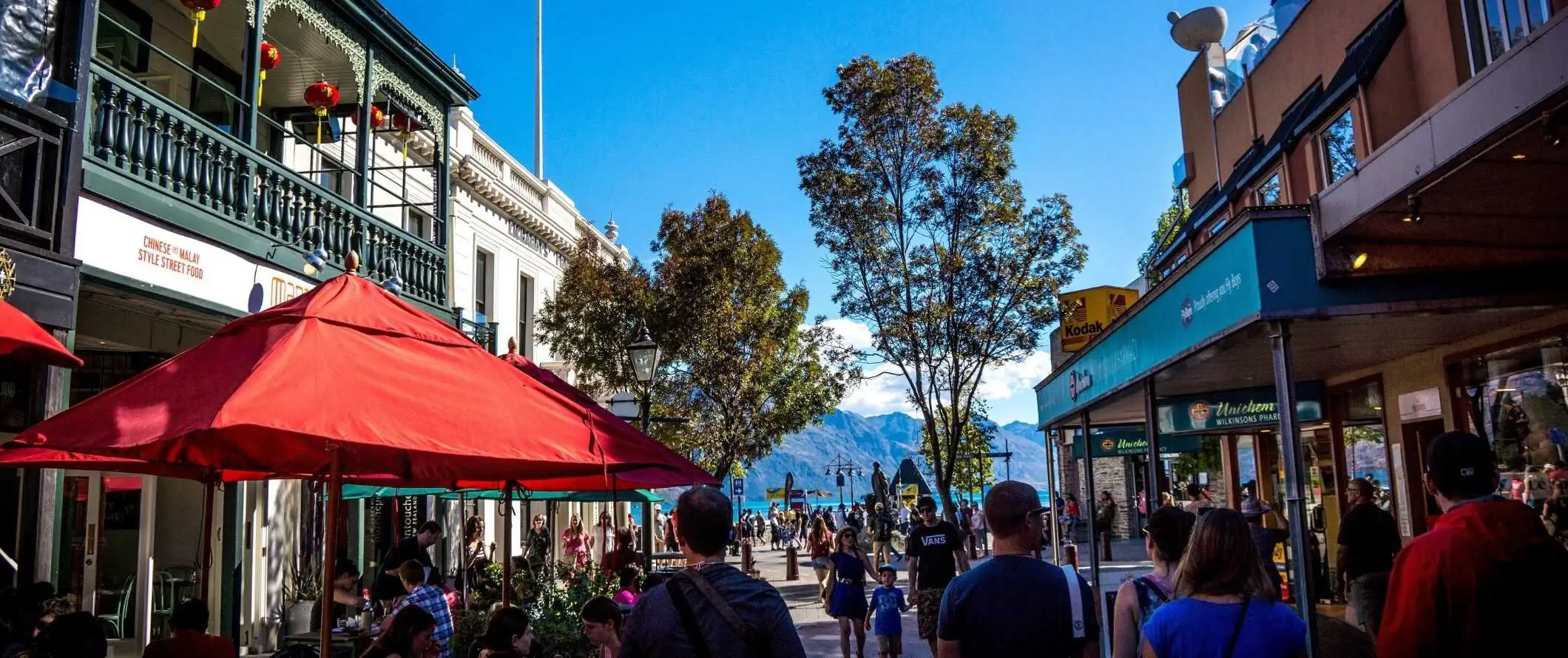 Folk som går nedover gaten i historiske Queenstown, New Zealand, med innsjøen og fjellene i bakgrunnen