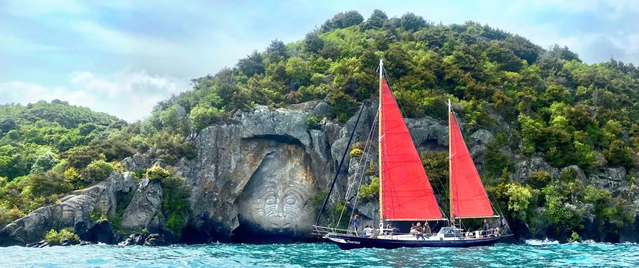 Velero pasando por tallas rupestres maoríes en el lago Taupo en Nueva Zelanda.