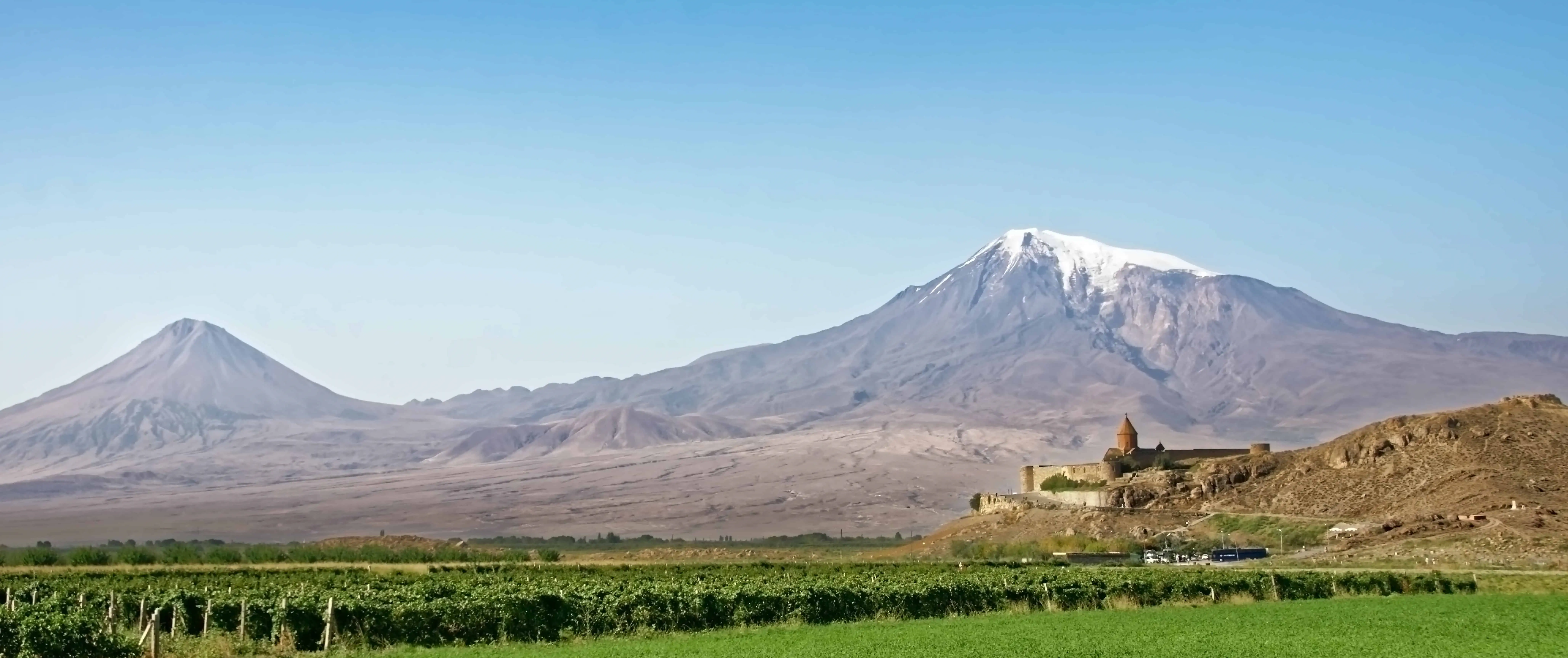 Paisatge ampli amb vinyes, un monestir i una muntanya al fons a Armènia